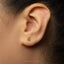 A close-up of a person's ear with a small gold earring featuring the number 6.