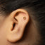A close-up of a person's ear with a small gold hexagonal stud in the earlobe.