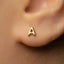 A close-up of a person's ear with a small gold letter earring featuring the letter 'A' in the center.