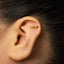 A close-up of a person's ear with a gold earring featuring a spiral design.