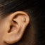 A gold-colored earring with a small figure on it is shown in the image.