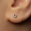 A close-up of a person's ear with a small silver hexagonal earring in the earlobe.