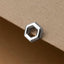 A silver hexagonal earring is resting on a brown surface.
