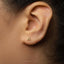 A close-up of a person's ear with a small gold letter earring featuring the letter 'A' in the center.