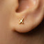 A close-up of a person's ear with a small gold earring featuring a letter 'X' in the center.