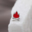 A small silver pin in the shape of a red fire on a white surface.
