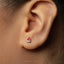 A close-up of a person's ear with a small, red earring featuring a flame design.