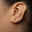 A close-up of a person's ear with a small gold earring featuring a bird design.