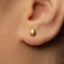 A close-up view of a person's ear with a small gold earring in the earlobe.