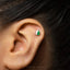 A close-up of a person's ear with a small, green and white earring in the earlobe.