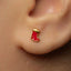 A close-up of a person's ear with a small red earring in the earlobe.