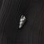 A small silver shell-shaped charm is attached to a black fabric surface.