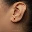 A close-up of a person's ear with a small red earring in the earlobe.