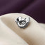 A silver-colored metal object, possibly a piece of jewelry, is resting on a white fabric surface.