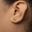 A close-up of a person's ear with a small gold heart-shaped earring in the earlobe.