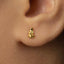 A close-up of a person's ear with a small gold earring in the earlobe.