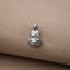 A small silver pendant in the shape of a seated Buddha figure is resting on a beige fabric surface.