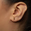 A close-up of a person's ear wearing a small gold earring with a small, intricate design.