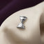 A silver hourglass-shaped brooch is resting on a beige fabric surface.