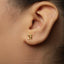 A close-up view of a person's ear wearing a small gold-colored earring.