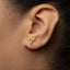 A close-up of a person's ear with a small gold earring featuring a gymnast performing a handstand pose.