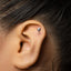 A close-up of a person's ear with a small silver earring in the shape of a wine glass.