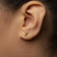 A close-up of a person's ear with a small gold earring featuring a small animal design.