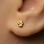 A close-up of a person's ear with a small gold earring featuring a hand-like symbol, likely representing the Hamsie symbol.