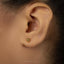 A close-up of a person's ear with a small gold earring featuring a cat's head design.