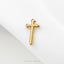 A small gold cross pin is placed on a white fabric surface.