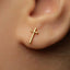 A close-up of a person's ear with a small gold cross earring.