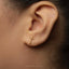 A close-up of a person's ear with a small gold cross earring.