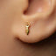 A close-up of a person's ear with a small gold earring featuring a small charm hanging from it.