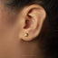 A close-up of a person's ear with a small gold earring in the earlobe.
