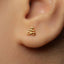 A close-up of a person's ear with a small gold earring featuring an intricate design.