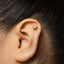 A close-up of a person's ear with a small gold-colored earring featuring a small animal design.
