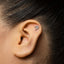 A close-up of a person's ear with a small silver tree-like earring in the earlobe.