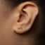 A close-up of a person's ear with a small gold-colored earring featuring a bicycle design.