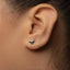 A close-up of a person's ear with a small silver earring featuring a small silver bird or winged design.
