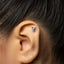 A silver earring with a small cat-like figure attached to the earlobe.