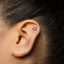 A close-up of a person's ear with a small silver earring featuring a red cherry design.