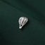 A small silver pin shaped like a hot air balloon is resting on a dark green fabric.