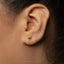 A close-up of a person's ear with a small gold earring featuring a hot air balloon design.