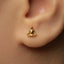 A close-up of a person's ear wearing a small gold earring with a small Buddha-like symbol on it.