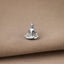 A small silver-colored pendant in the shape of a seated Buddha figure is resting on a beige fabric surface.