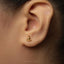 A close-up of a person's ear wearing a small gold earring with a small Buddha-like symbol on it.