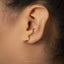 A close-up of a person's ear with a gold snake-shaped earring attached.