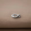 A silver fish-shaped pendant is resting on a beige fabric surface.