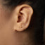 A close-up view of a person's ear with a small gold earring featuring a fish design.