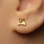 A close-up view of a person's ear wearing a small gold earring with a small car-like design.